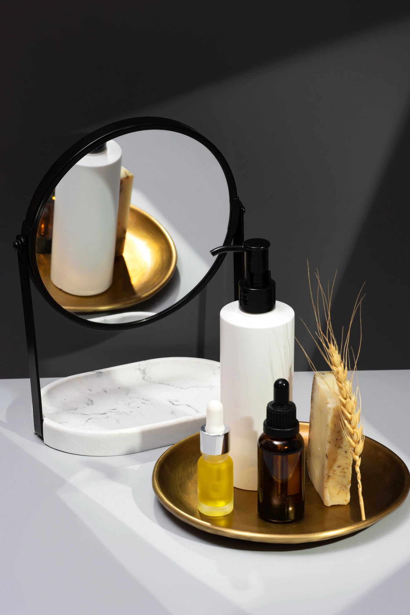 Naturaleza muerta editorial con cosméticos y espejo sobre fondo gris oscuro